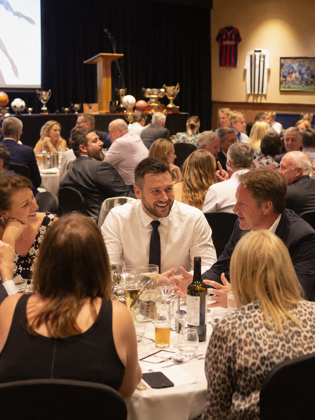 Guests at an awards night dinner with trophies on stage