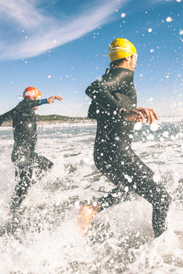Two men in wetsuits running into the ocean waves