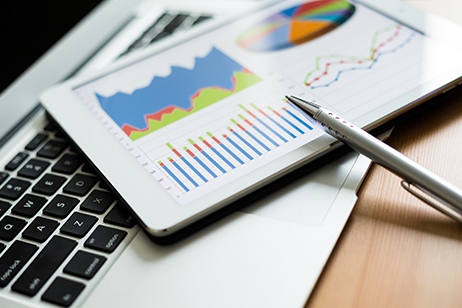 pen and ipad containing business charts resting on top of laptop