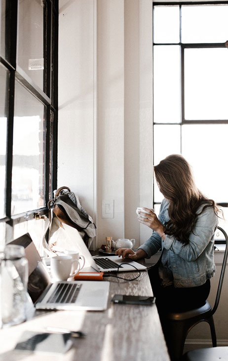A woman working while holding a cup in front of her laptop