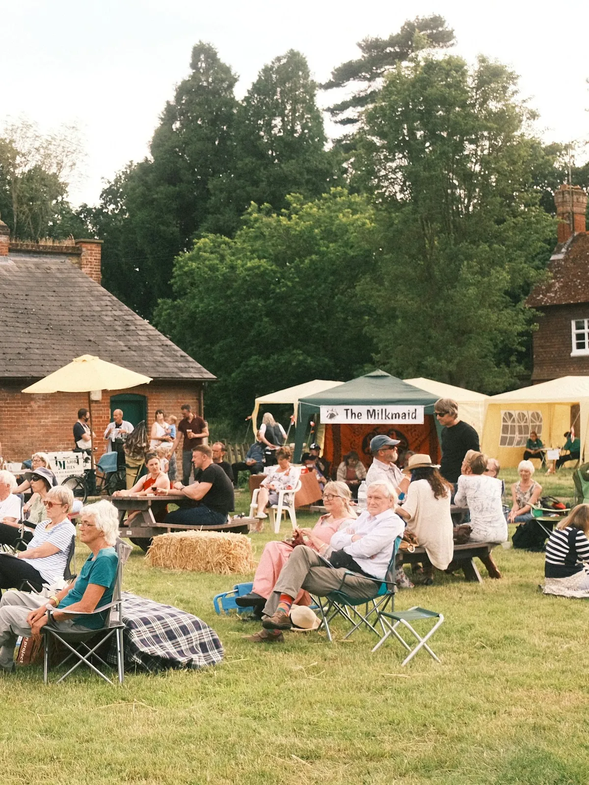 Families at a village green summer fete with gazebos, hay bales and picnic benches