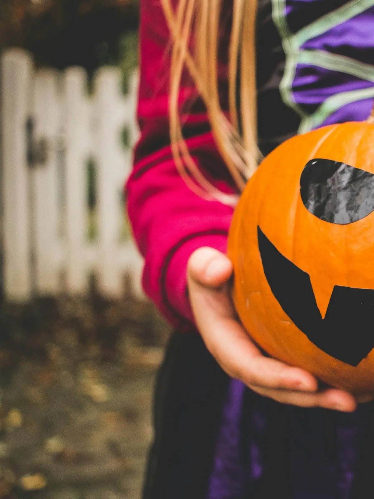 A child in a witch costume holding a carved pumpkin